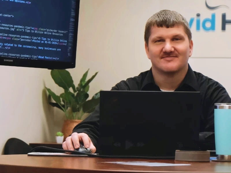 Ryan sitting at a desk with a computer in front of him and code on a monitor stand
